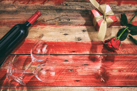 Valentines day concept. Red wine bottle, glasses and a gift on red wooden backgroundの写真素材
