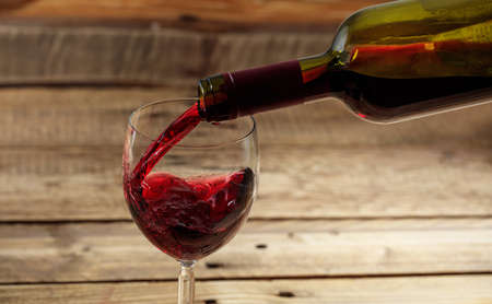 Pouring red wine in a glass on a wooden tableの写真素材