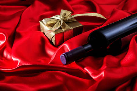 Valentines day concept. Red wine bottle and a gift box on red silk textileの写真素材