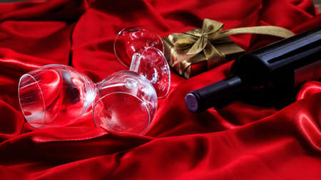 Valentines day concept. Red wine bottle, glasses and a gift box on red silk textileの写真素材