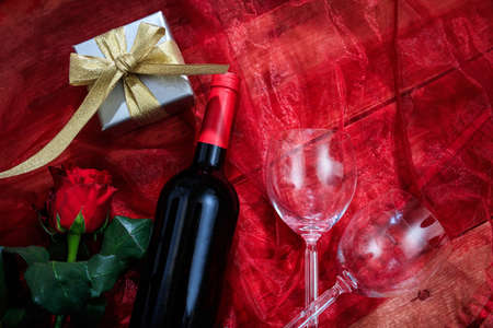 Valentines day concept. Red wine bottle, glasses and a gift box on red textileの写真素材