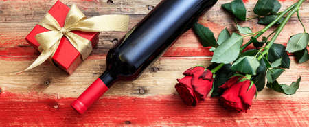 Valentines day concept. Red wine bottle, roses and a gift on wooden backgroundの写真素材