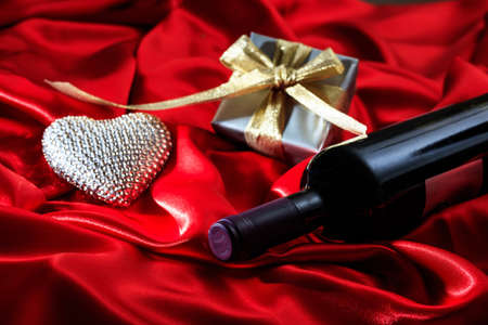 Valentines day concept. Red wine bottle, a gift box and a heart on red silk textileの写真素材