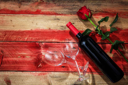 Valentines day concept. Red wine bottle, glasses and a rose on red wooden backgroundの写真素材