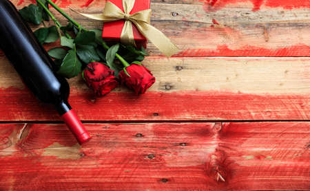 Valentines day concept. Red wine bottle, roses and a gift on wooden backgroundの写真素材