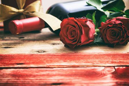 Valentines day concept. Red wine bottle, roses and a gift on wooden backgroundの写真素材