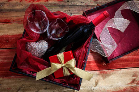 Valentines day concept. Red wine bottle, glasses and a gift in a box, wooden backgroundの写真素材