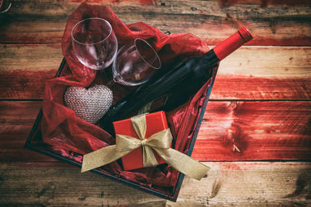 Valentines day concept. Red wine bottle, glasses and a gift in a box, wooden background with copyspaceの写真素材