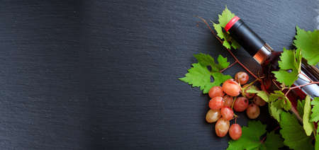 Rose wine bottle and fresh grape leaves on black background, top view, copy spaceの写真素材