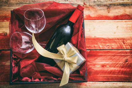 Valentines day concept. Red wine bottle, glasses and a gift in a box, wooden background with copyspaceの写真素材