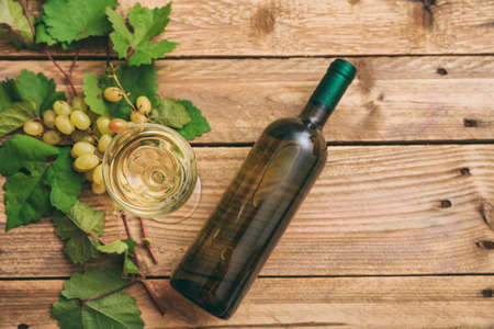 White wine glass and bottle and fresh grapes on wooden background, top view, copy spaceの写真素材