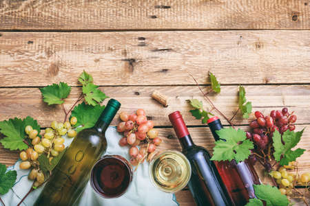 Red and white wine glasses and bottles on wooden background. Fresh grapes and grape leaves as decoration, top view, copy spaceの写真素材