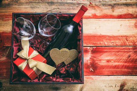 Valentines day concept. Red wine bottle, glasses and a gift in a box, wooden background with copyspaceの写真素材