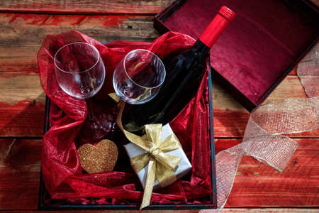 Valentines day concept. Red wine bottle, glasses and a gift in a box, wooden backgroundの写真素材