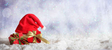 Red Christmas gift boxes and santas hat on abstract cold winter background with snowの写真素材