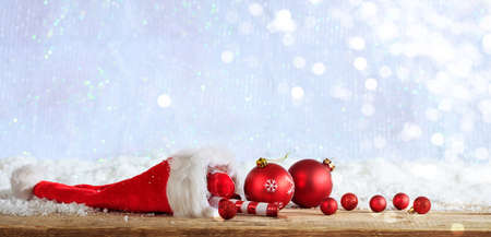 Red Christmas ornaments and santas hat on wooden snowy backgroundの写真素材