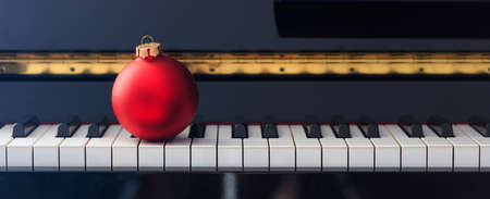 Red Chritmas ball on classical piano keyboard, front viewの写真素材