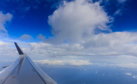 Fluffy white clouds on a blue sky from a plane window background. Space for text.の写真素材