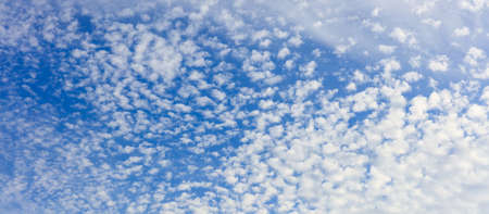 Blue sky with white scattered clouds backdrop.の写真素材