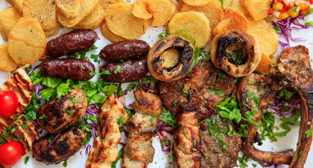 Cypriot delicacies. Mixed grilled meat with vegetables and potatoes on white surface. Close up view.の写真素材