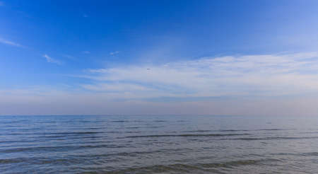 Calm clear sea and blue sky with white clouds background. An airplane fly on the horizon.の写真素材