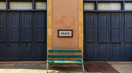 Word peace framed above an old wooden bench on a column between two locked doors. Close up view.の写真素材