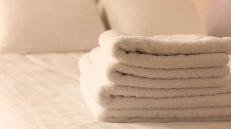 Hotel bedroom. White fluffy, folded towels, linen beddings on tidy bed. Close up view, details.の写真素材