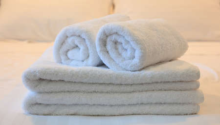 Hotel bedroom. White rolled and folded towels, white beddings backdrop. Close up view, details.の写真素材