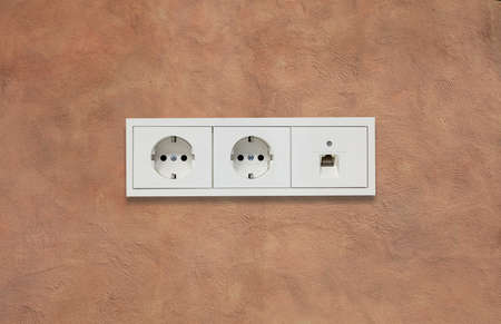Double modern electric sockets and network line. Light brown stucco wall backdrop. Closeup, details.の写真素材