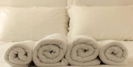Hotel bedroom. White fluffy, rolled towels in row, linen beddings on tidy bed. Close up view.の写真素材