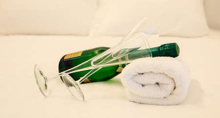 A bottle of champagne and two glasses laying on white towel. White bedding background, closeup view.の写真素材