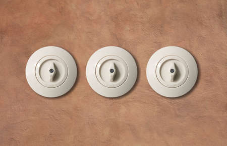 Three switches vintage round with button from porcelain isolated on light brown stucco wall. Close up, detail.の写真素材