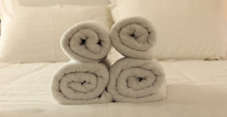 Hotel's bedroom. White fluffy, rolled towels, linen sheets and pillows on a tidy bed. Closeup.の写真素材