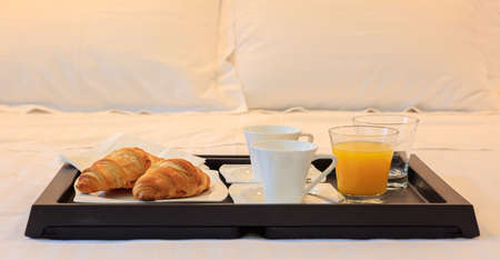 Continental breakfast in bed of hotel. Closeup view of tray with croissants, coffee and juice. Blurred white pillows backdropの写真素材