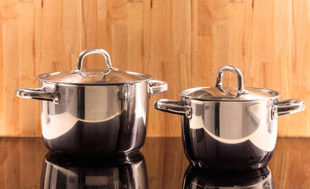 Traditional cooking pots placed on ceramic hob. Wooden background. Reflection, close up, details.の写真素材