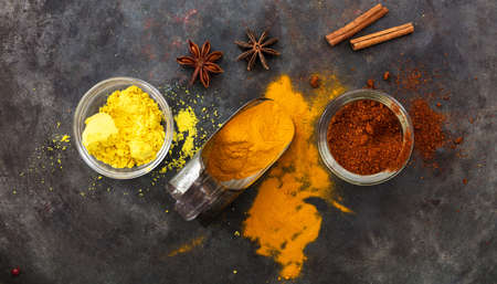 Spices with bright colors and an old metal scoop on metal rusty background, top view