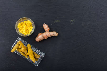 Fresh and dried turmeric or curcumin roots and powder on black background. Top view, copy spaceの写真素材