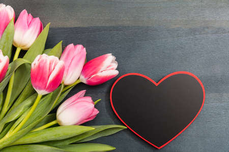 Valentine's day. Pink tulips bouquet and a blank heart shape board on blue wooden background, copy space, top viewの写真素材