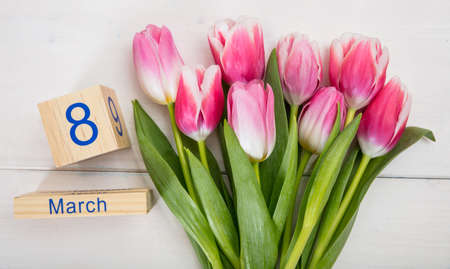 Women's day concept. Pink tulips bouquet and the March 8th date on white wooden background