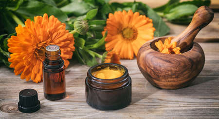 Calendula products. Essential oil, ointment and a mortar on a wooden table, fresh blooming calendula background,の写真素材