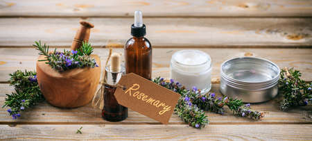 Rosemary aromatherapy. Essential oil and cosmetics, fresh blooming twig in a mortar, tag with text rosemary, banner. Wooden table backgroundの写真素材