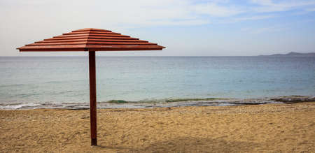 Wooden umbrella on an empty sandy beach. Blue sky and calm sea background, copy spaceの写真素材