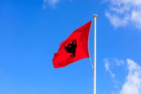 Albania flag. Albanian flag on a flagpole waving in an opposite direction on a blue sky backgroundの写真素材