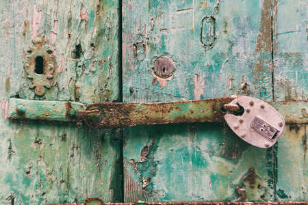 Locked door. Closed old rusty padlock on a damaged wooden door, closeup viewの写真素材