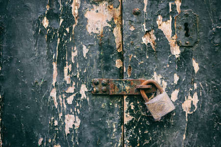 Locked door. Closed old rusty padlock on a damaged wooden door, closeup view