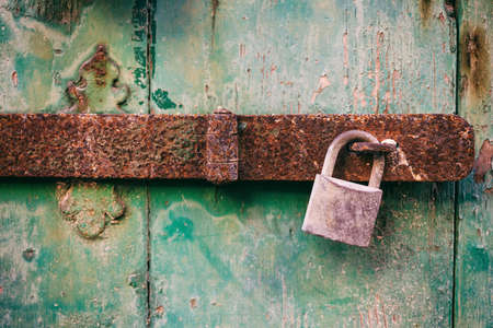 Locked door. Closed old rusty padlock on a damaged wooden door, closeup view