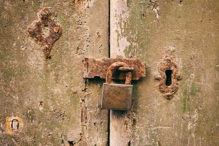 Locked door. Closed old rusty padlock on a damaged wooden door, closeup viewの写真素材