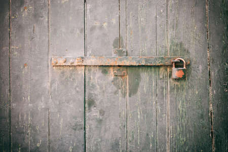 Locked door. Closed old rusty padlock on a weathered wooden door, closeup viewの写真素材