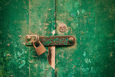 Locked door. Closed old rusty padlock on a damaged wooden door, closeup viewの写真素材
