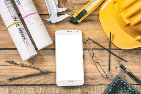 Architect workplace. Smart phone with white blank screen, project construction blueprints and...